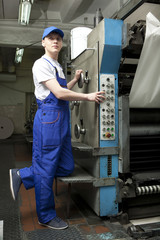 Young man in cap working on offset printing machine
