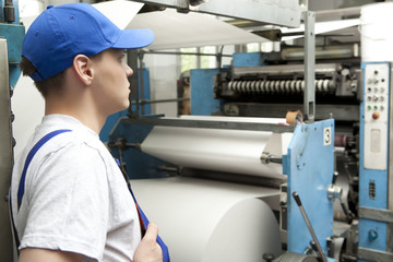 Young man in cap working on offset printing machine