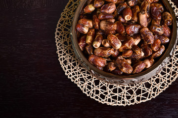 Date fruits in a deep round dish on a black wooden background.