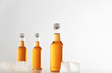Three sealed bottles with cold cider drink inside isolated on white between ice cubes, presentation mockup