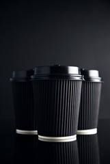 Luxury set of black take away cardboard paper cups closed with caps isolated on black and mirrored. Space for your text above
