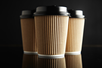 Three take away cardboard paper cups closed with caps isolated on black and mirrored. Retail mockup presentation
