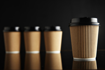 One focused coffee take away cardboard paper cup ahead others unfocused, all closed with black caps presented on black and mirrored. Retail mockup presentation