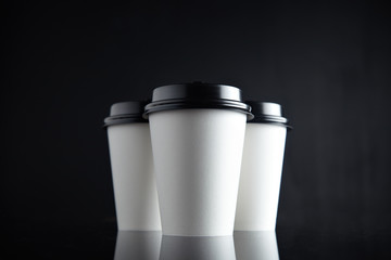 Set of three take away white coffee cardboard paper cups closed with black caps isolated in center and mirrored. Retail mockup presentation