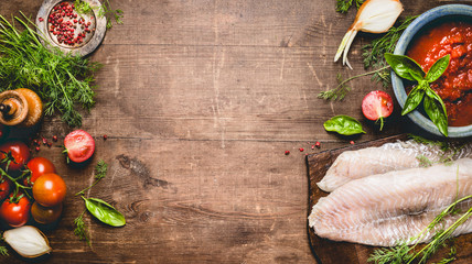 Fish dishes cooking. Fresh raw fish fillet with tomatoes ,sauce and ingredients on rustic wooden background, top view, banner. Healthy or diet food concept