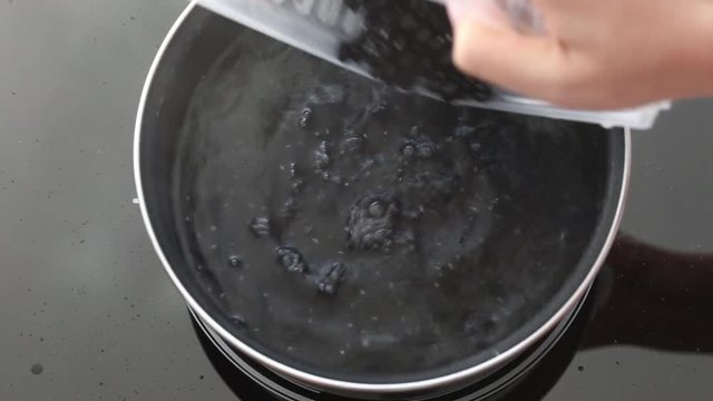 Woman throw red beans at pan with boiling water on Induction stove