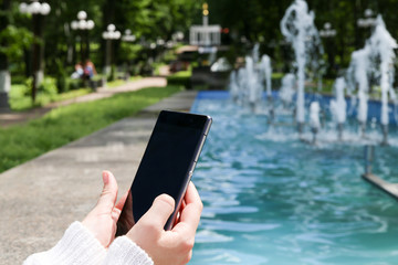 Closeup of female hand using a smart phone in a park