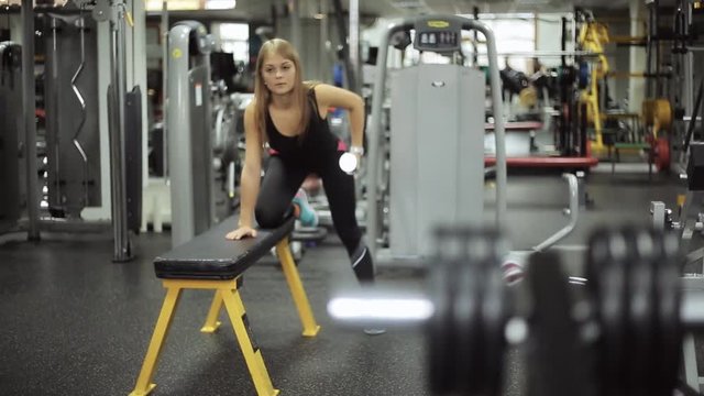Smooth focus on a woman engaged in gym with dumbbells at bench.