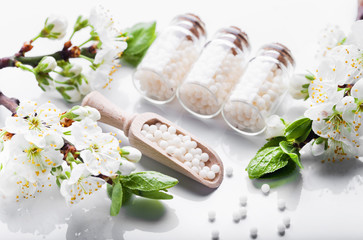 homeopathic pills with spring flowers on white wooden background