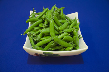 Fresh green peas in white dish on a blue background