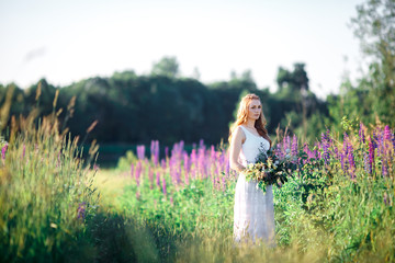 Fototapeta na wymiar Beautiful young woman over blooming lupines with bunch of flowers in hands