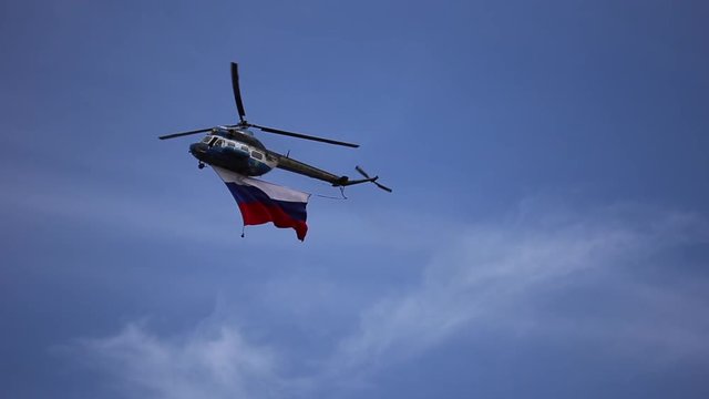 The helicopter flies with the flag of Russia on blue sky background
