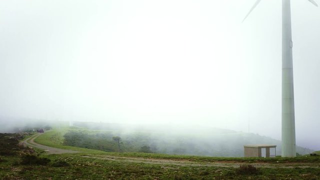 Empty landscape of nature on top of mountain with tourbine towers. Thick fog and strong wind blows the clouds across uneven road Group of friends arrived by car to explore on left side