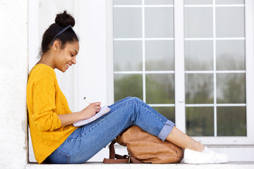 Happy young woman sitting outdoors writing a book