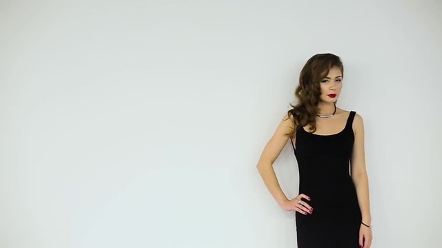 Beautiful girl in black dress posing on a white background.