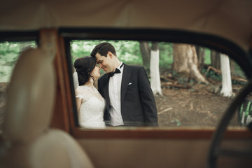 Beautiful newlywed couple posing near retro black car