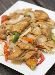 Thai food for lunch in a plate on a wooden table. Fried noodles with fish, red pepper and greens. 