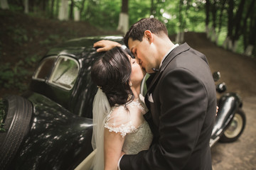 Beautiful newlywed couple posing near retro black car