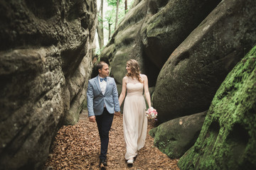 Gorgeous wedding couple kissing and hugging in forest with big rocks