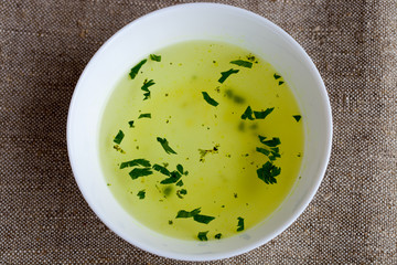Clear soup in a white cup on the natural burlap