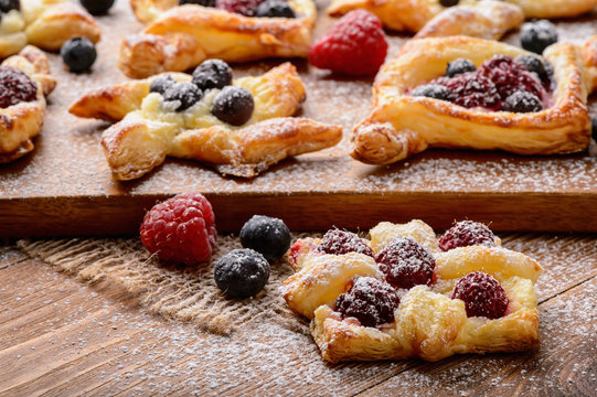 Puff pastries with raspberries, blueberries and cream cheese on wooden background.