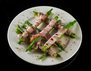 asparagus fried in bacon in a white plate on a black background