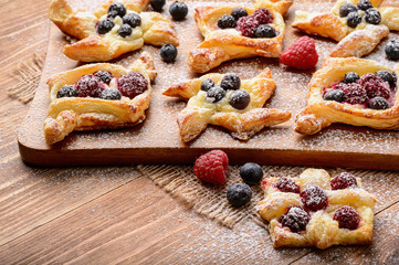 Puff pastries with raspberries, blueberries and cream cheese on wooden background.