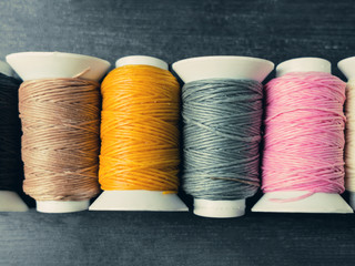 Black, brown, yellow, grey, pink and white thread rolls on a woo