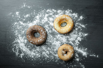 donuts with icing sugar on black wooden background.
