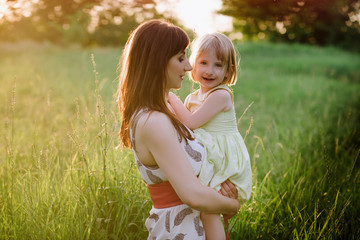 Mom kisses and hugs daughter on nature in sunset light, family, motherhood, child
