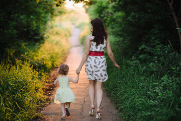 Obraz premium Mom keeps daughter's hand and walks the walk on the nature in sunset light, motherhood, child, family