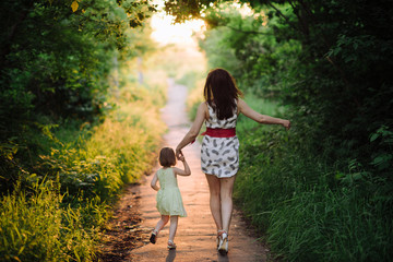 Mom keeps daughter's hand and walks the walk on the nature in sunset light, motherhood, child, family