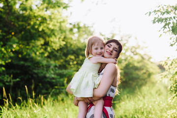 Fototapeta premium Mom kisses and hugs daughter on nature in sunset light, family, motherhood, child