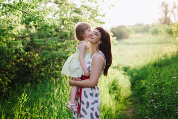 Mom kisses and hugs daughter on nature, family, motherhood, child