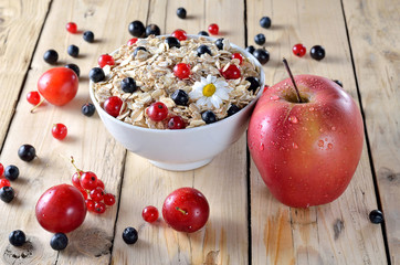 Oatmeal with berries and fresh apple on a wooden table.