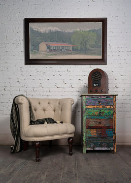 Composition of vintage beige armchair, colorful cupboard, aged wooden radio and hanged painting