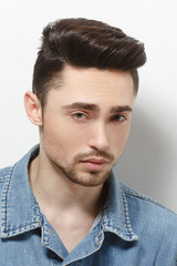 Obraz premium Portrait of young model man demonstrating his gorgeous and luxurious hair in studio. Handsome male in jeans shirt over shite background.