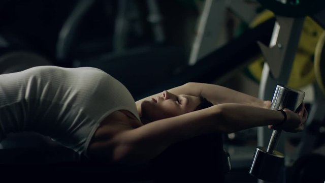 Woman doing a Dumbbell Pullover exercise on a bench in a gym.
