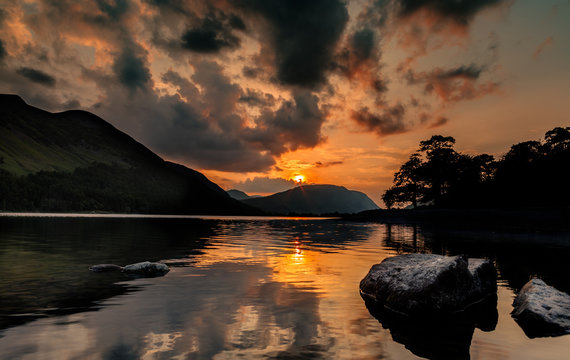 Orange Sunset Clouds Reflected on Calm Water Surface of Buttermere Lake in Cumbria, UK
