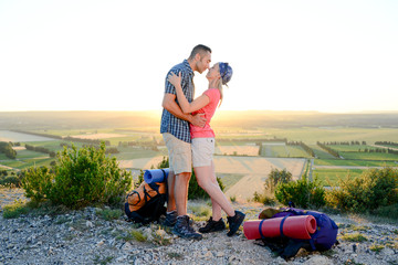 young couple with backpack on adventure mountain trek admiring a beautiful sunset landscape