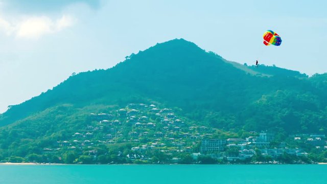 Video 1080p - Tourist, enjoying the view from high altitude as he parasails under a cheerful, rainbow colored parachute over the tropical sea in Southeast Asia.