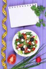 Greek salad with vegetables, centimeter and notepad for notes, healthy food and slimming concept