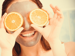 Woman with mud facial mask holds orange slice