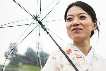 Young attractive Japanese woman in kimono holding an umbrella on a rainy day