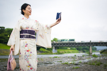 Young attractive Japanese woman in kimono taking selfie with cellphone outside