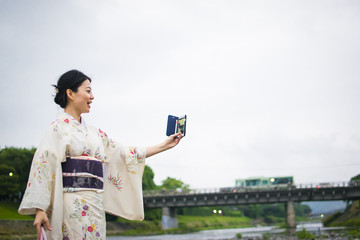 Young attractive Japanese woman in kimono taking selfie with cellphone outside