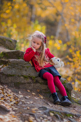 sad girl sitting on a rock in the autumn forest with a favorite toy in the hands of