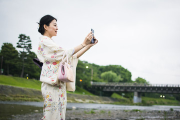 Young Japanese Woman In Kimono Taking Photos With Cellphone Outdoors