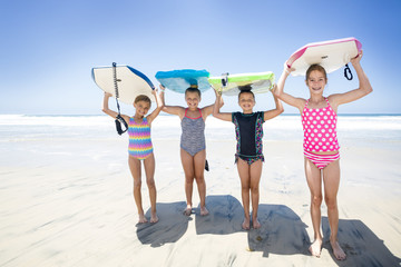 Kids playing at the beach together while on vacation holding their boogie boards