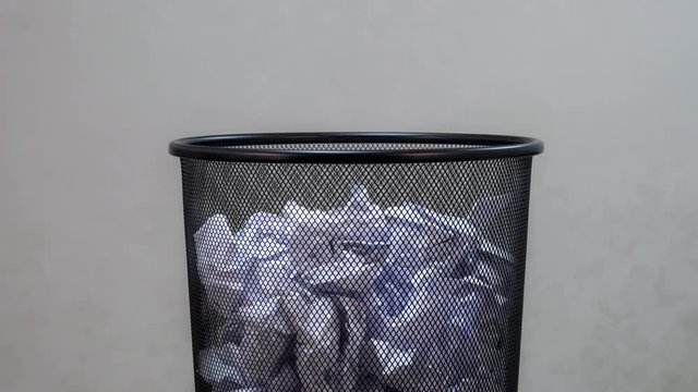 An empty office trash basket gets filled up with waste papers. Stop motion